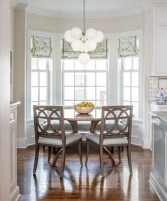 a dining room table surrounded by chairs in front of two windows