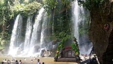 people standing in front of a waterfall with a wooden bench on the ground near it