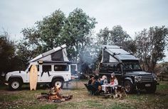 two people sitting around a campfire with their van in the background