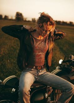 a woman sitting on the back of a motorcycle in a grassy field with her hands behind her head