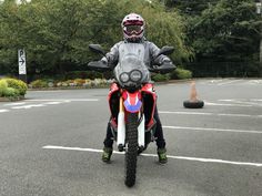 a man riding on the back of a red motorcycle in a parking lot next to trees