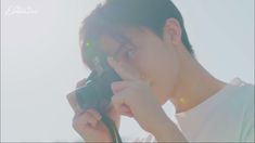 a young man holding a camera up to his face while looking into the distance with sunlight shining on him