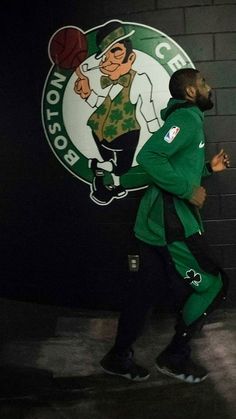 a man in a green jacket and black pants is walking past a boston basketball logo