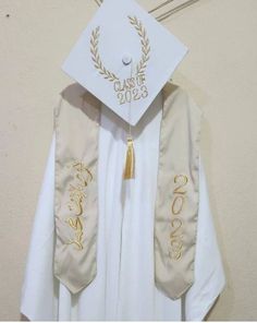 a white graduation gown with gold lettering on the front and back, hanging from a wall