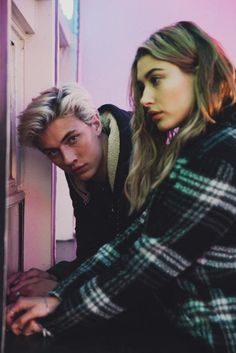 a young man and woman leaning against a wall looking at each other's eyes