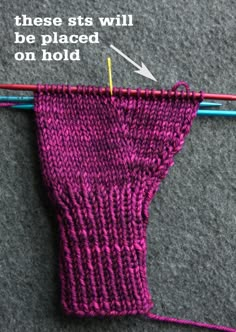 a pair of knitting needles are next to a purple knitted mitt that has been stitched together