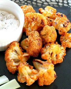 some cauliflower and celery on a black plate with a small white bowl