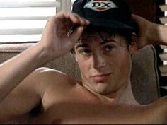 a shirtless young man sitting in a chair with his hat on top of his head