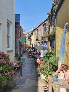 people sitting at tables in an alleyway with colorful flags hanging from the buildings behind them