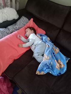 a baby sleeping on top of a brown couch next to a pink and blue blanket