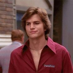 a young man in a red shirt is walking down the street with his hands in his pockets