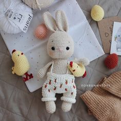 a crocheted bunny doll sitting on top of a bed next to balls of yarn