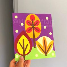 a hand holding up a card with trees on it in front of a door and purple background