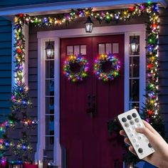 a hand holding a remote control in front of a house decorated with christmas lights and wreaths