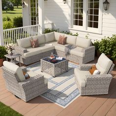 an outdoor living area with wicker furniture and rugs on the decking next to a white house