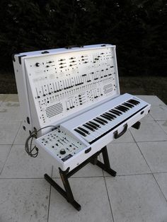 an electronic keyboard sitting on top of a white tile floor next to a black stand