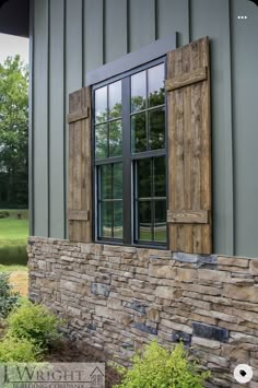 an old window with wooden shutters on the side of a stone wall in front of a green building