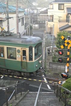 a green train traveling down tracks next to buildings