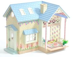 a doll house with a blue roof and flowers on the walls, sitting next to a potted plant