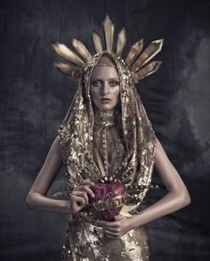 a woman dressed in gold and holding a red heart with feathers on it's head