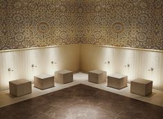 an artisticly designed bathroom with three urinals in the middle and four boxes on the floor