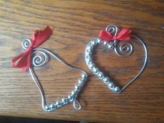 two metal heart ornaments with red bows on top of a wooden table next to each other