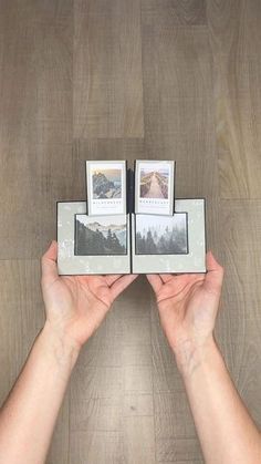 two hands holding three small photos on top of a wooden table next to each other