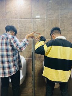 two men standing next to each other near a urinal in a public restroom,