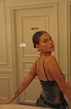 a woman standing in front of a mirror with her hands behind her back and the words ok above her head