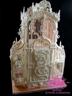 an elaborate white birdcage with intricate carvings on the doors and sides is shown