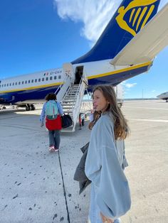 a woman standing in front of an airplane on the tarmac with her back to the camera