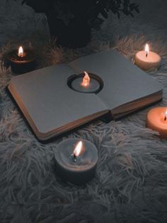 an open book sitting on top of a fur covered floor next to lit candle holders