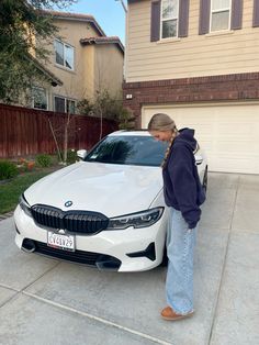 a woman standing next to a white car in front of a house