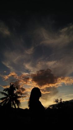 the silhouette of a person standing in front of a sunset with palm trees and clouds