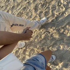 two people sitting on the beach with their feet in the sand