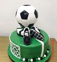 a soccer themed cake with shoes and a ball on top, sitting on a table