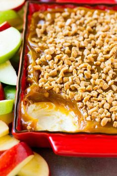 an apple dessert with nuts and caramel on top in a red dish next to sliced apples