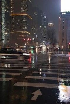 a city street at night with cars driving on the road and buildings in the background