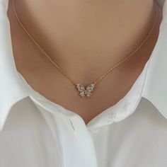 a woman wearing a white shirt and gold necklace with two butterflies on it's neck