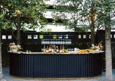 an outdoor bar with lots of bottles and glasses on the counter, surrounded by trees