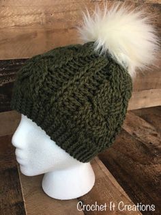 a green hat with white fur pom - poms on top of a mannequin head