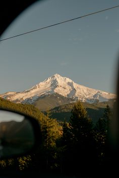 a view of a snow covered mountain in the distance from a car's side mirror