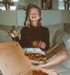 a woman sitting on a couch holding two pizzas in front of her face and smiling at the camera