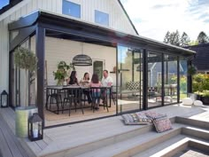 three people sitting at a table on the back deck of a house with sliding glass doors