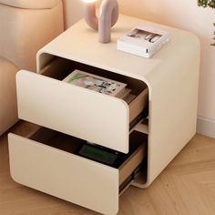 a white table with two drawers and a vase on it's side stand next to a couch