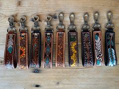 six leather key fobs are lined up on a wooden table with metal hooks