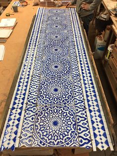 a blue and white tile work bench being worked on in a shop with people standing around