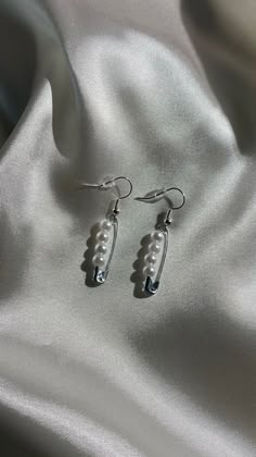 a pair of earrings with pearls hanging from them on a white satin surface, close - up