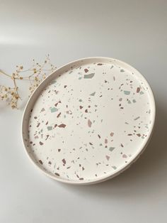 a white plate with speckles on it next to a flower vase and dried plant