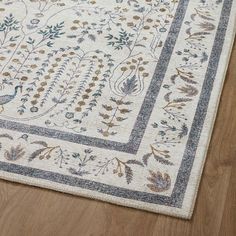 a white rug with blue and gold designs on the bottom is laying on a wooden floor